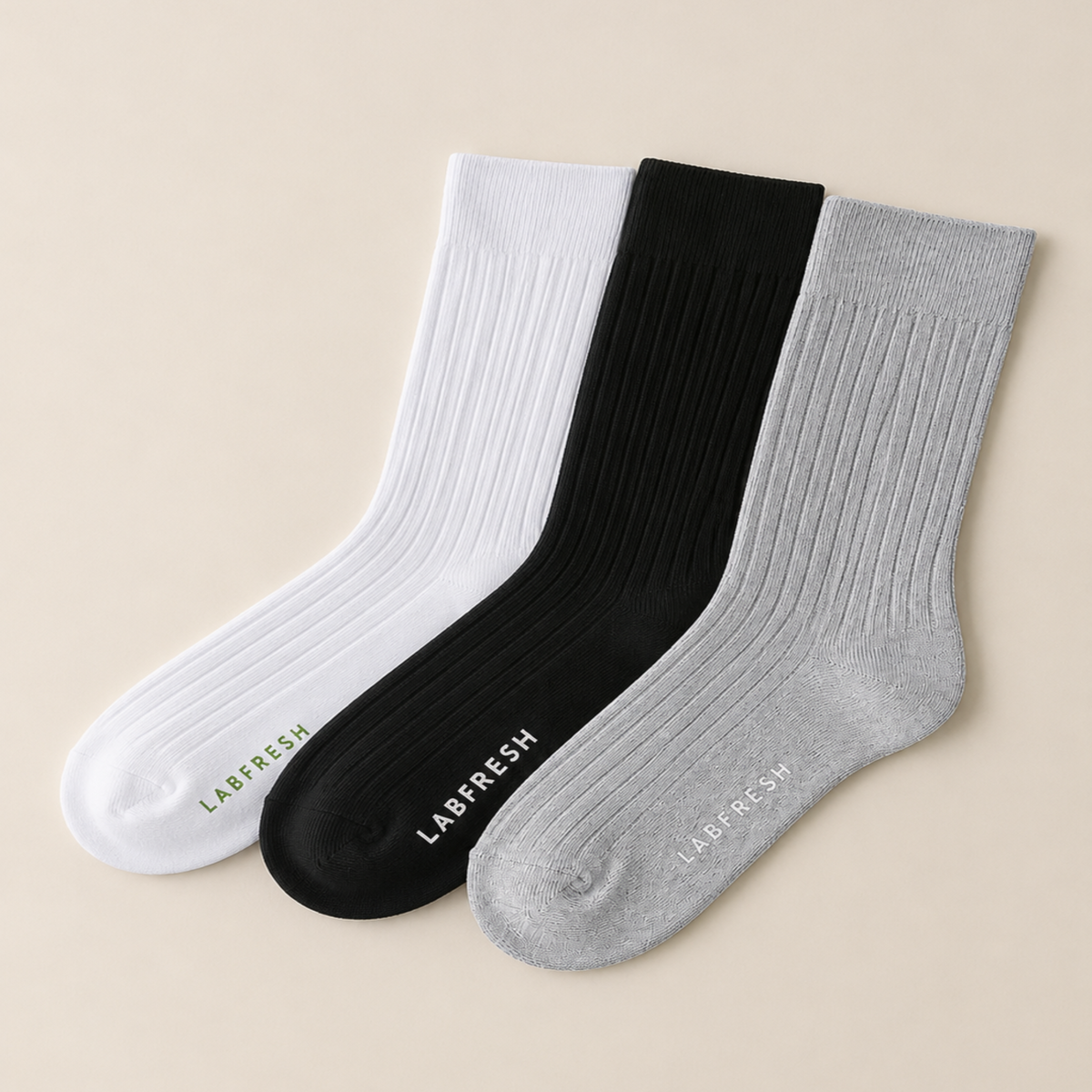 Three ribbed crew socks in white, black, and light gray, arranged diagonally on a light beige background. Each sock has the LABFRESH brand name printed on the sole.